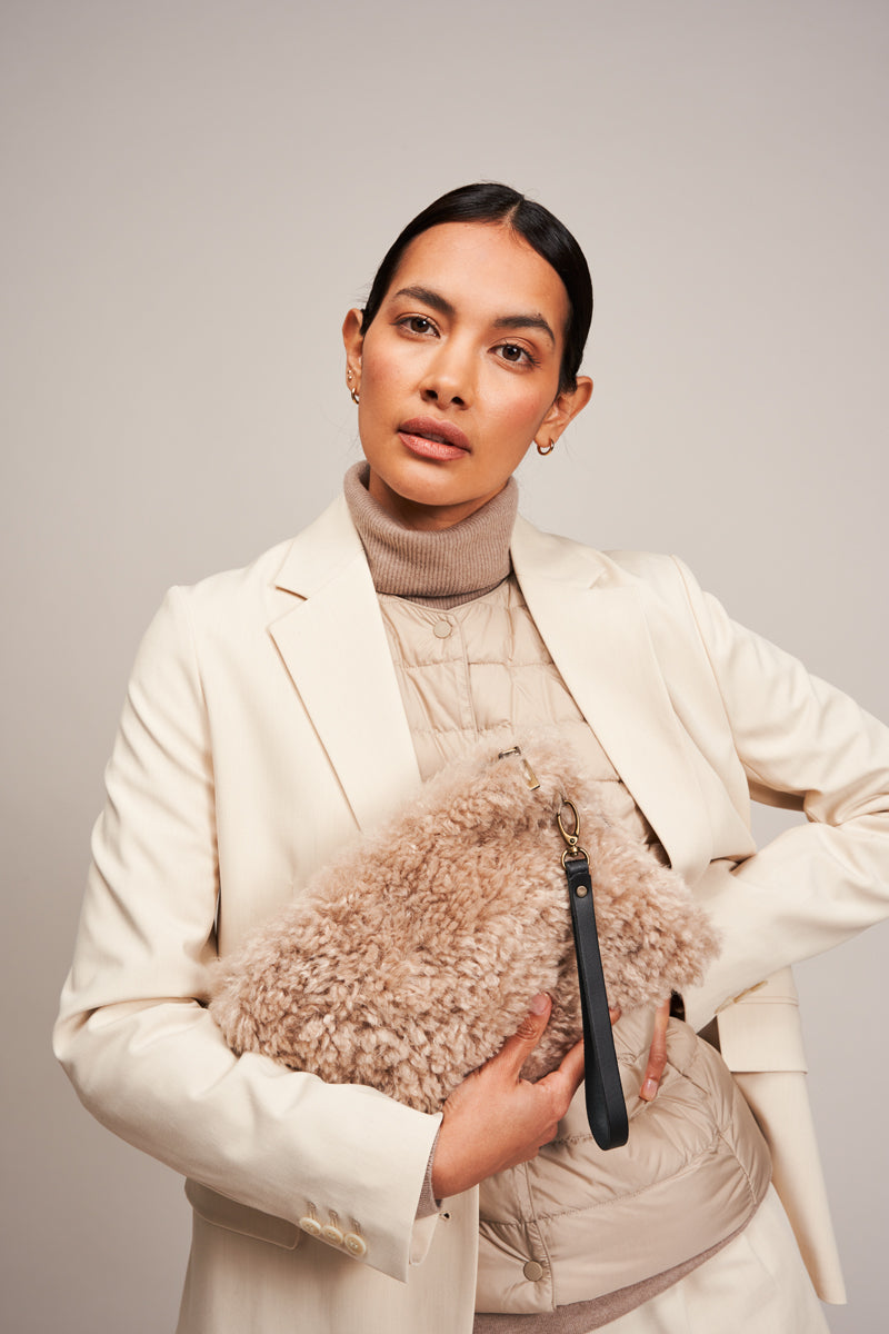 Model holding the Pebble cream faux sheepskin clutch bag with leather wrist strap by Helen Moore.